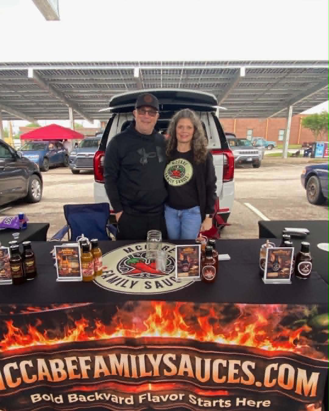 Lee McCabe and a family member behind the McCabe Family Sauces table at a farmers market